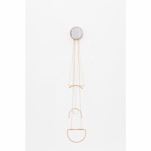 May include: A gold metal wall-mounted jewelry organizer with a circular mirror and multiple hanging chains and geometric shapes.