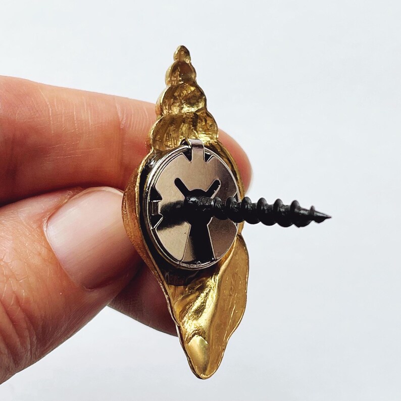 May include: Gold seashell wall hook with a screw and a metal backing. The hook is designed to look like a seashell.