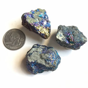 May include: Three iridescent pyrite stones with a blue, purple, and gold sheen. The stones are rough and have a natural, unpolished look. They are arranged on a white background.