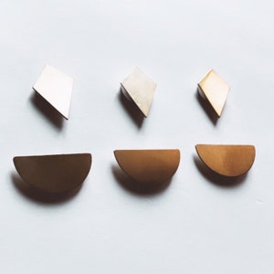 May include: Three pairs of earrings in different shapes and colors. The first pair is a silver diamond shape, the second pair is a gold diamond shape, and the third pair is a gold half-circle shape.