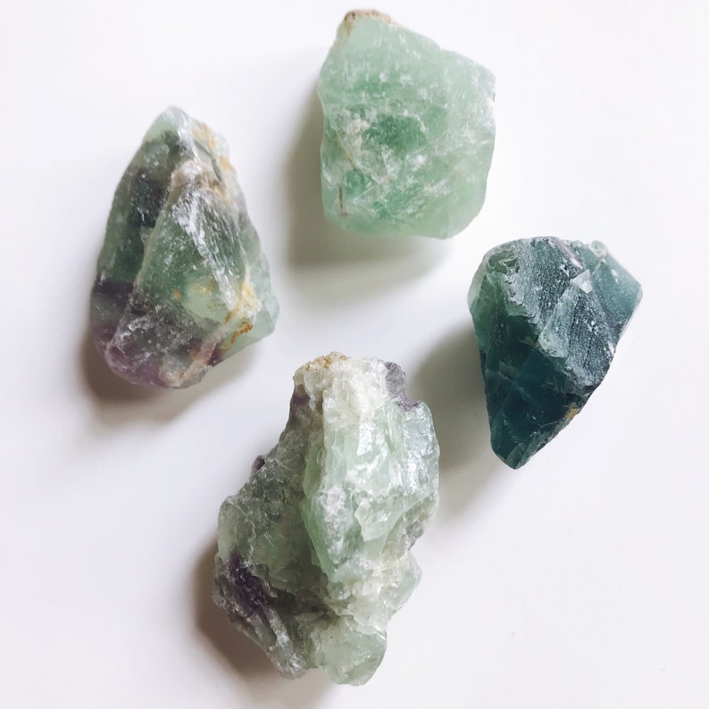 May include: Four green fluorite crystals with varying shades of green and purple. The crystals are rough and have natural edges.