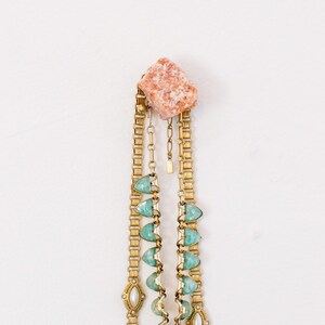 May include: A gold chain necklace with green and white stones and a pink stone charm.