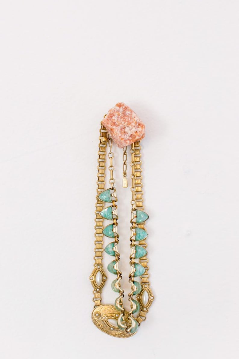 May include: A gold chain necklace with green and white stones and a pink stone charm.