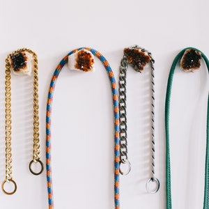 May include: Four different types of leashes for dogs, each with a crystal charm. The leashes are a gold chain, a colorful rope, a silver chain, and a green rope.