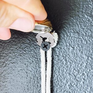 May include: A close-up of a silver metal wick holder with a black screw. The wick holder is attached to two white wicks.