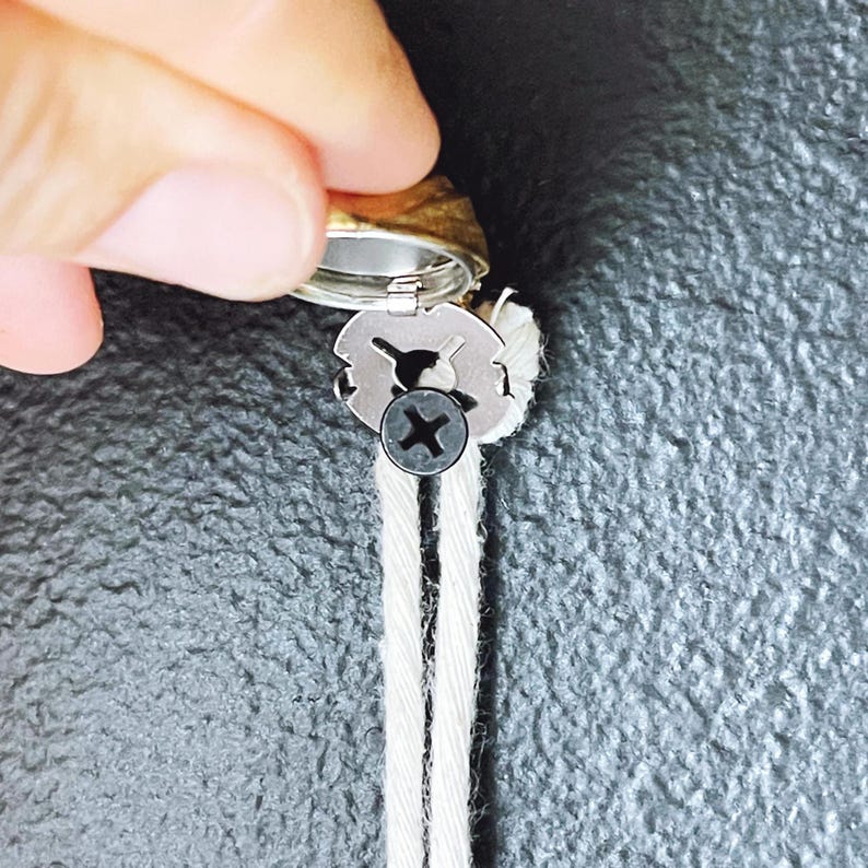 May include: A close-up of a silver metal wick holder with a black screw. The wick holder is attached to two white wicks.