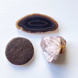 May include: Three natural objects: a brown and black agate slice, a light brown and white stone, and a dark brown fur circle.