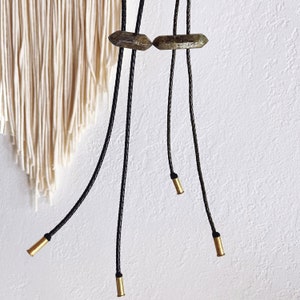 May include: A pair of black leather cord necklaces with green stone pendants. The necklaces have gold-colored metal tips at the ends.