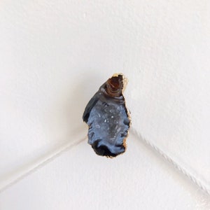 May include: A gold-rimmed agate slice with a black and white interior. The agate is a natural stone with a unique pattern.