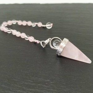 Può includere: Un pendolo di cristallo di quarzo rosa con una sfera di cristallo trasparente e una catena d'argento. Il pendolo è attaccato a una catena di perline rosa e trasparenti.