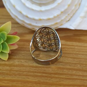 May include: A silver ring with a geometric design. The ring is made of metal and has a flower of life pattern.