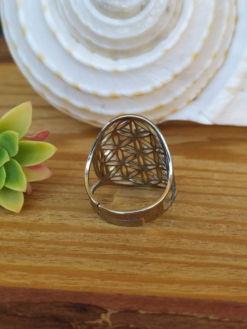 May include: A silver ring with a geometric design. The ring is made of metal and has a flower of life pattern.