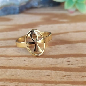 Pode incluir: Um anel dourado com um design de símbolo Ankh. O anel está sobre uma superfície de madeira.