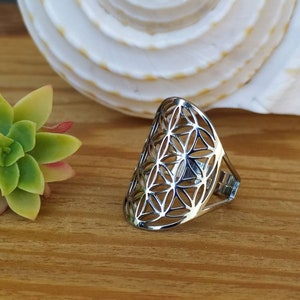 May include: A silver ring with a geometric flower of life design. The ring is open and has a curved shape.