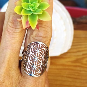 May include: A silver ring with a flower of life design. The ring is on a person's finger.