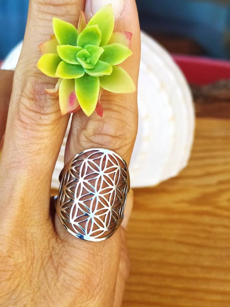 May include: A silver ring with a flower of life design. The ring is on a person's finger.