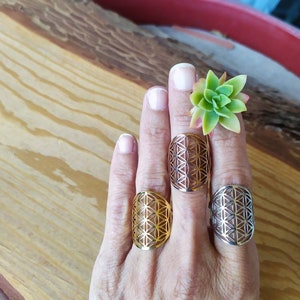 May include: Three silver rings with a geometric flower of life design. The rings are on a person's fingers.