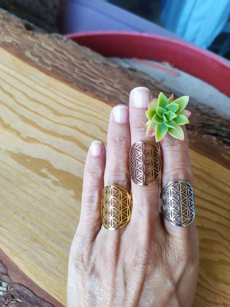 May include: Three silver rings with a geometric flower of life design. The rings are on a person's fingers.