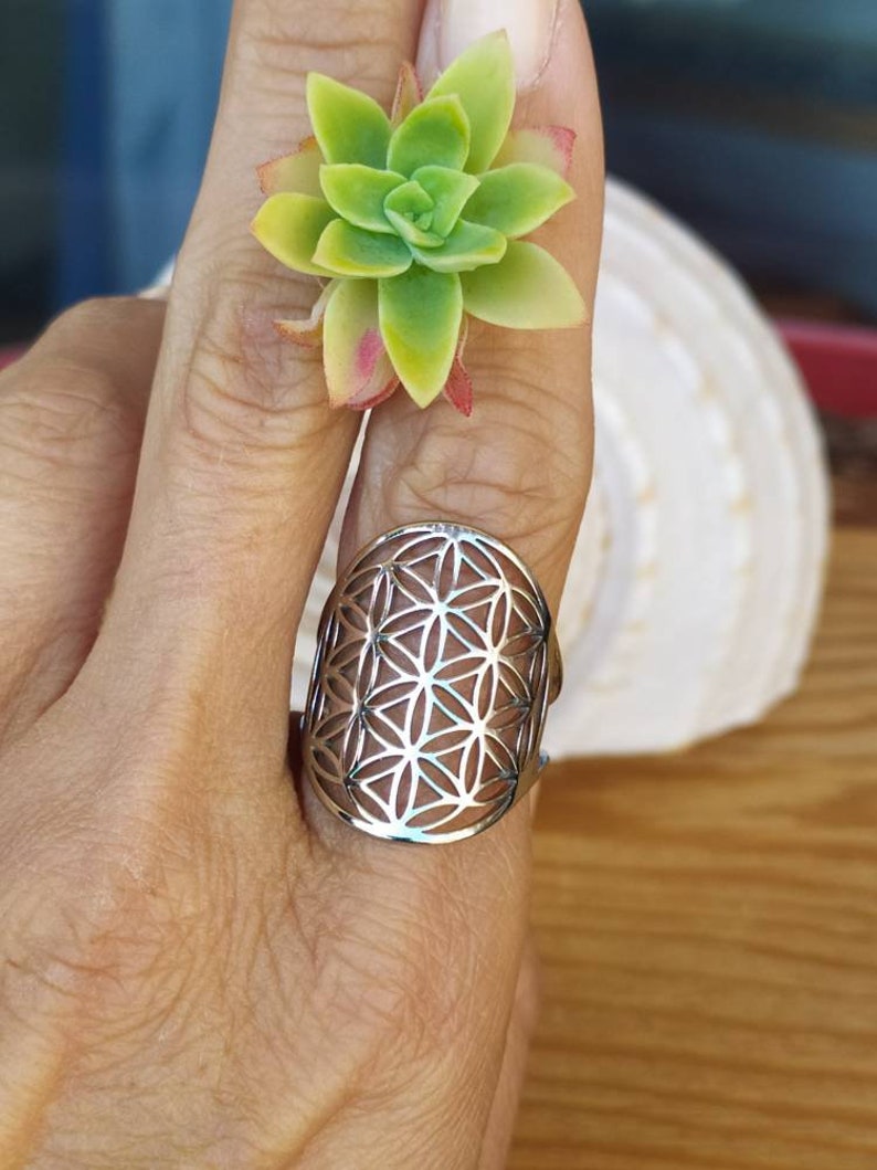May include: A silver ring with a geometric flower of life design. The ring is worn on a finger.