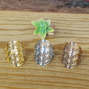 May include: Three silver rings with a geometric flower of life design. The rings are on a wooden surface.
