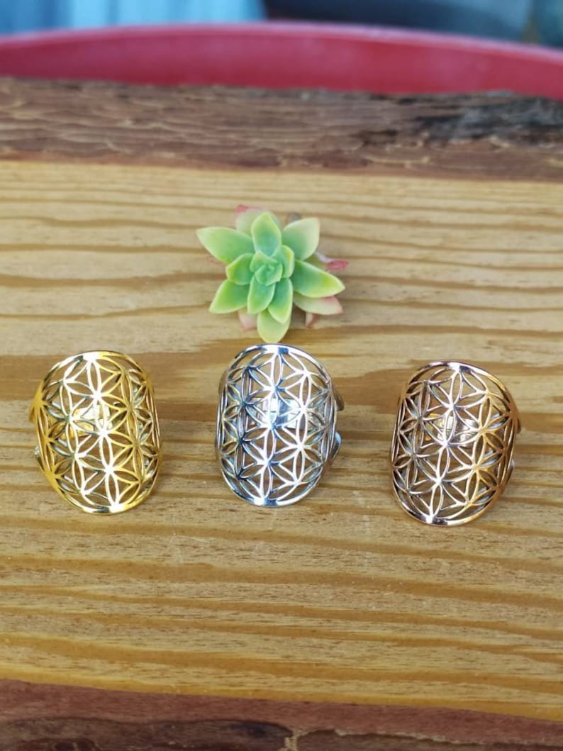 May include: Three silver rings with a geometric flower of life design. The rings are on a wooden surface.
