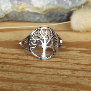 Puede incluir: Un anillo de plata con un diseño de árbol de la vida. El anillo está sobre una superficie de madera.