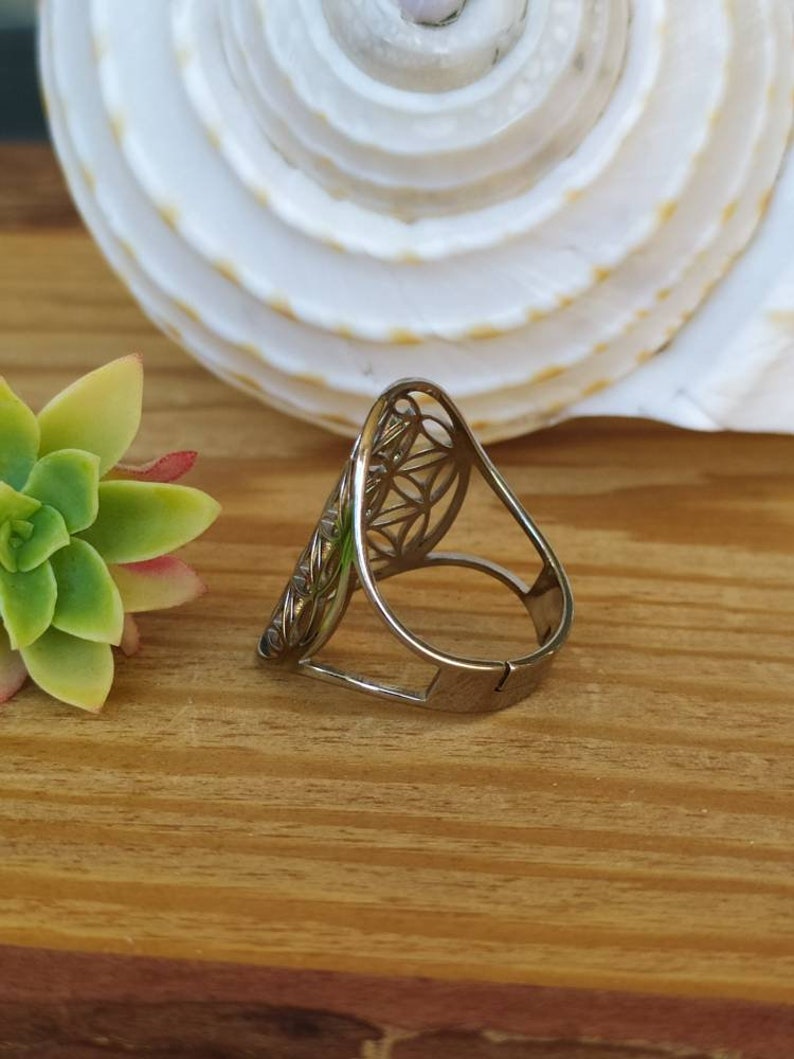 May include: A silver ring with a geometric design. The ring is open and adjustable.
