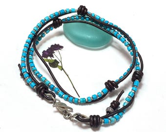 May include: A turquoise and silver beaded bracelet with brown leather cord and a silver clasp. The bracelet is wrapped around a piece of turquoise glass.
