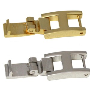 May include: Two watch clasps, one gold-toned and one silver-toned, are displayed. The clasps are open, revealing their hinge and locking mechanisms. Each clasp has an 'H' shaped design.