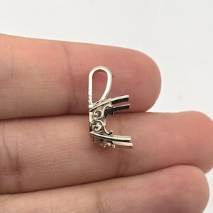 May include: A silver-toned metal pendant setting featuring a decorative scrollwork gallery and a vertical bail at the top. The setting includes four prongs extending outward, designed to hold a gemstone, with a polished metallic finish throughout.