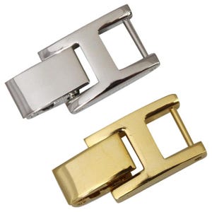 May include: Two metal watch clasps. One is silver-colored, the other is gold-colored. Both clasps have a rectangular shape with a hinged section and a bar for closure. The clasps are designed for watch bands or similar accessories.