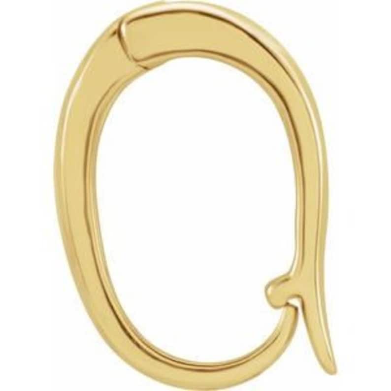 May include: A gold-colored, abstract-shaped pendant. The pendant has a curved, elongated oval design with a hook-like extension at the bottom. The surface appears smooth and reflective, suggesting a polished finish. The overall design is minimalist and modern.