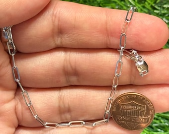 Può includere: Una collana a catena color argento con maglie rettangolari e una chiusura. Una moneta di rame da un centesimo è accanto alla catena per il confronto delle dimensioni. La catena è tenuta in una mano su uno sfondo verde.
