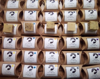 May include: A display of handmade goat's milk soap bars in various scents, including lavender, rosemary and lemon, and citrus and thyme. The bars are wrapped in brown paper and labeled with the scent and "Handmade Goat's Milk Soap".