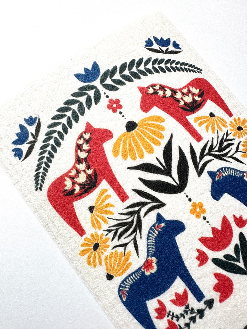 May include: A white background with a pattern of red and blue stylized horses, green leaves, and yellow and red flowers. The horses are traditional Swedish Dala horses.