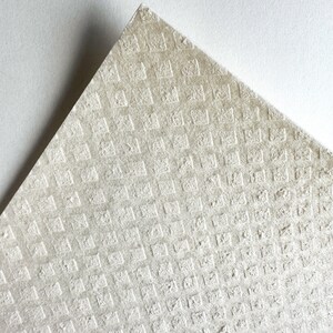 May include: A close-up of a textured, off-white surface with a repeating pattern of small squares. The surface is slightly rough and has a subtle sheen.