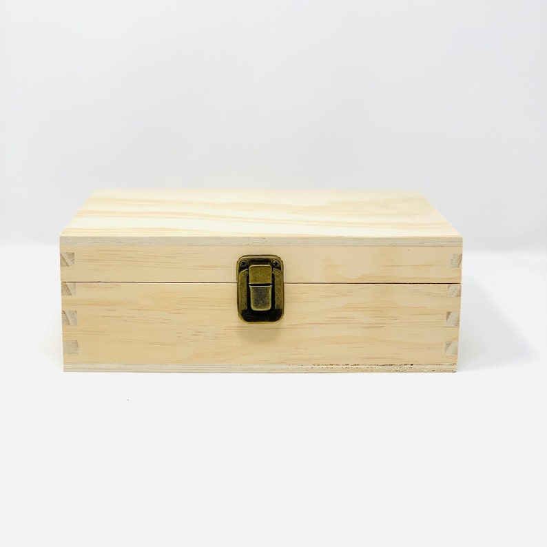 May include: A natural wood box with a brass latch. The box is closed and has a light wood grain.
