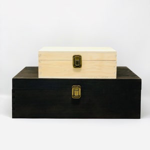 May include: Two wooden boxes stacked on top of each other. The top box is light wood with a brass latch. The bottom box is dark wood with a brass latch.
