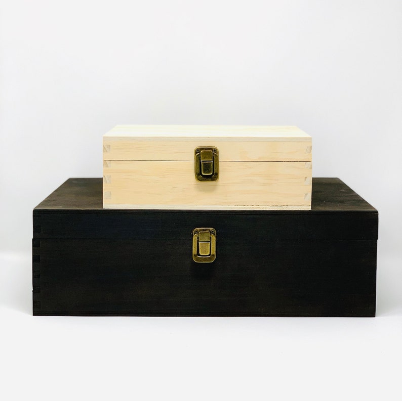 May include: Two wooden boxes stacked on top of each other. The top box is light wood with a brass latch. The bottom box is dark wood with a brass latch.