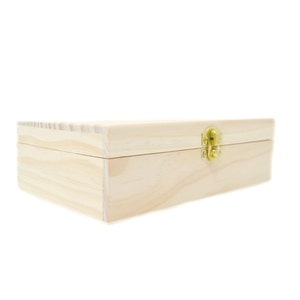 Op de afbeelding: Een eenvoudige houten doos met een scharnierend deksel en een messing sluiting. De doos is gemaakt van licht hout en heeft een natuurlijke afwerking.