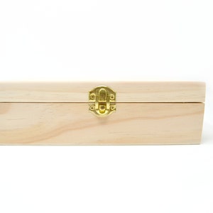 Op de afbeelding: Een houten doos met een scharnierend deksel en een messing sluiting. De doos is gemaakt van licht hout en heeft een natuurlijke afwerking.