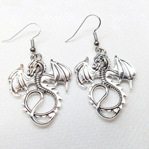 May include: A pair of silver dragon earrings with detailed wings and a curled tail. The earrings are hanging from silver hooks.