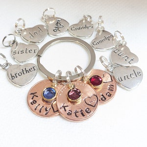 May include: A silver keychain with heart-shaped charms engraved with family member names like "dad", "mom", "sister", "brother", "aunt", "uncle", "grandma", and "grandpa".  The keychain also has three copper coins with a heart design and the names "Kelly", "Katie", and "Adam" engraved on them.  Each coin has a small gemstone embedded in the center.