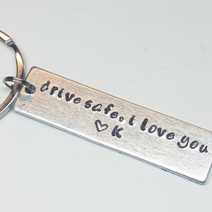 May include: Silver keychain with the text "drive safe. i love you" and a heart with the letter "K" engraved on it.