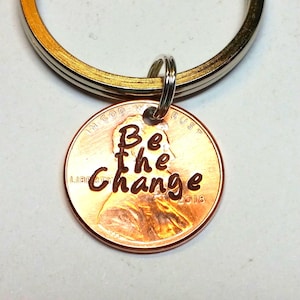 May include: A white ceramic mug with a black handle and the text "But First, Coffee" in a bold, black font. The mug is set against a blurred background, suggesting a cozy setting.