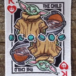 May include: A playing card featuring a green, cartoon character known as "The Child" from the Star Wars series, The Mandalorian. The card is a King of Hearts with the Star Wars logo in the heart.