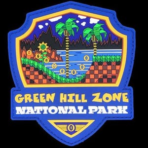 May include: A shield-shaped embroidered patch featuring a colorful landscape with palm trees, a blue river, and golden rings. The text reads GREEN HILL ZONE NATIONAL PARK in yellow and white lettering, with a small golden ring icon at the bottom.