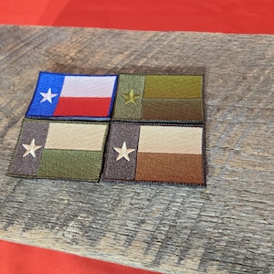 Puede incluir: Cuatro parches bordados con la bandera del estado de Texas en diferentes combinaciones de colores. Los parches están sobre una superficie de madera. Los parches son de color azul, blanco, rojo, verde y marrón.