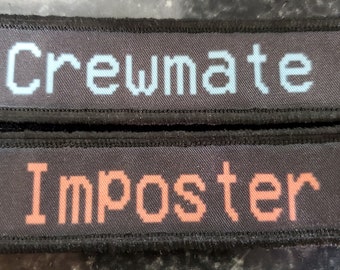 Könnte beinhalten: Zwei schwarze Stoff-Patches mit weißen Nähten an den Rändern. Der obere Patch hat das Wort "Crewmate" in hellblauem Pixeltext. Der untere Patch hat das Wort "Imposter" in orangefarbenem Pixeltext.