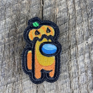 May include: Orange and black embroidered patch of a pumpkin-headed character from the video game Among Us.